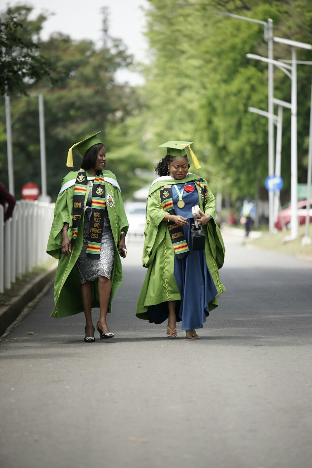 two women in graduation gowns walking down a street