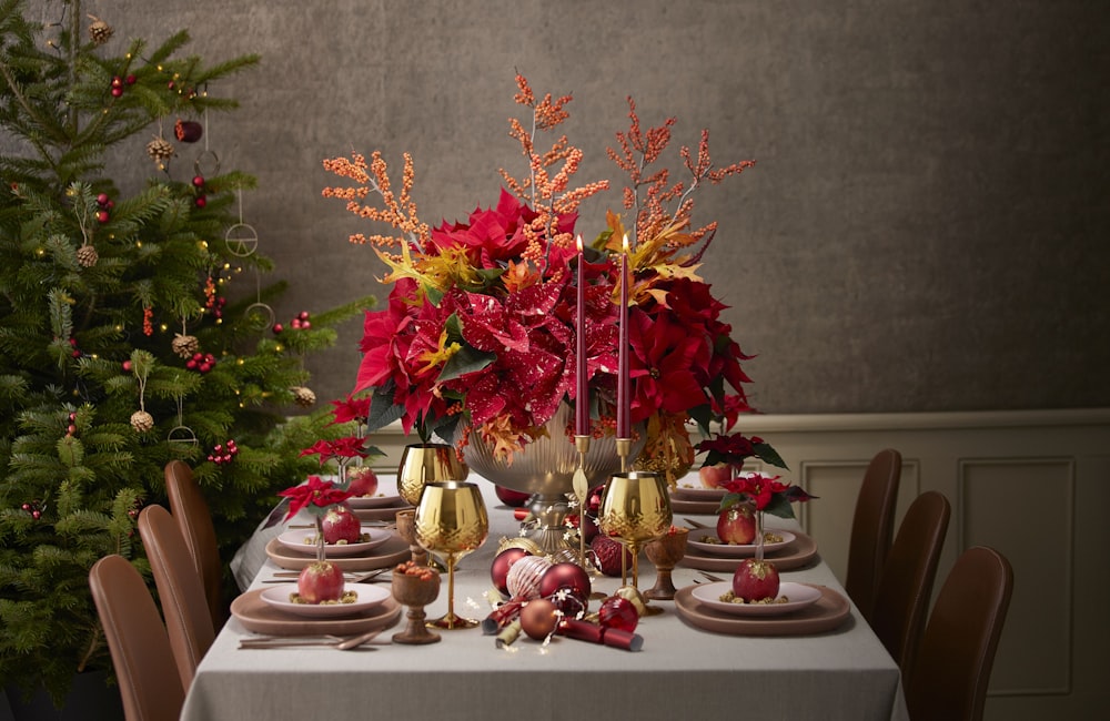 a table with a white table cloth and a silver vase filled with red flowers