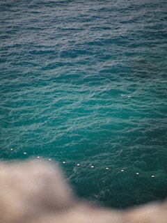 A vast expanse of ocean with layers of varying blue and green hues. The water's surface is textured with waves. A line of buoys forms a diagonal across the water, adding a sense of organization and boundary.