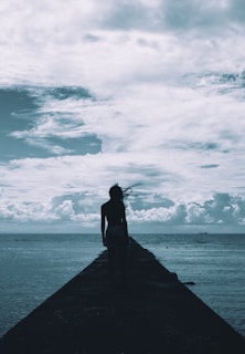 Wide shot of a solitary figure standing on a boat deck, gazing toward the vast sea under dramatic skies.