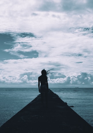 Wide shot of a solitary figure standing on a boat deck, gazing toward the vast sea under dramatic skies.