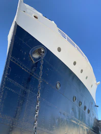 A close-up of a ship's hull being carefully painted with marine-grade coating under bright sunlight.