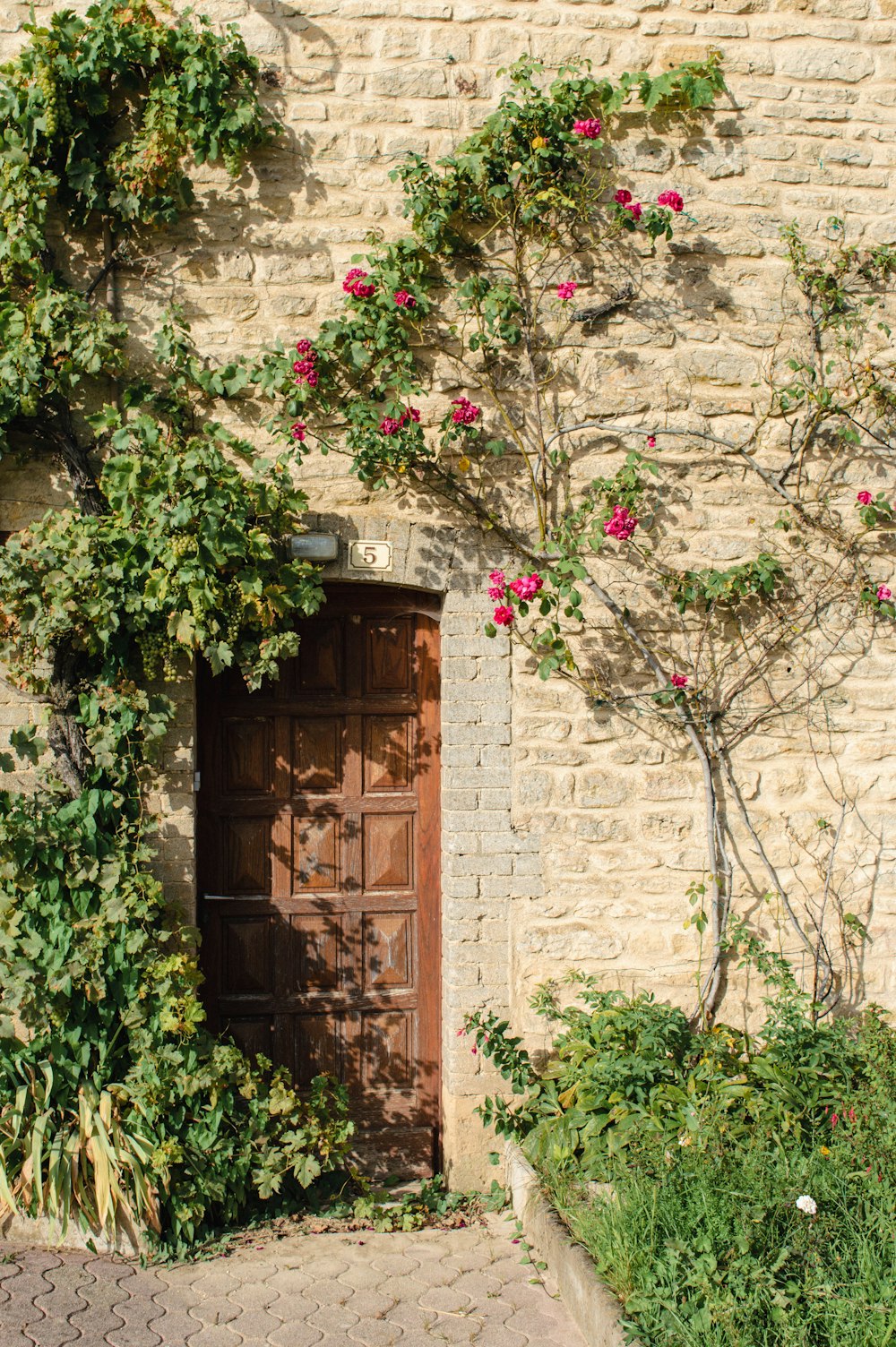 a brick building with a wooden door surrounded by flowers