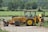 Photo of a satisfied farmer standing next to a mini excavator in a sunny field.