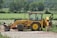 Photo of a satisfied farmer standing next to a mini excavator in a sunny field.