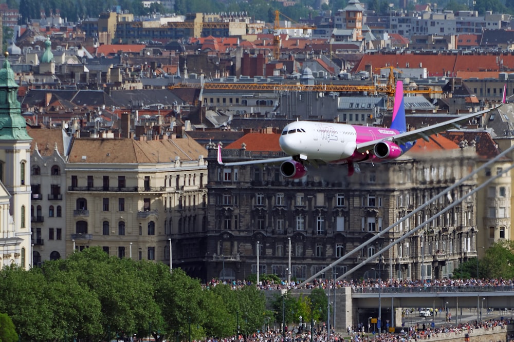 a pink and white plane flying over a city
