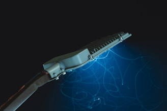 A streetlight with a sleek, modern design is emitting a blue glow in a dark environment. There are visible light trails beneath the lamp, creating an abstract, artistic effect.