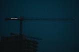 A sleek construction site at dusk with illuminated cranes against a black sky.