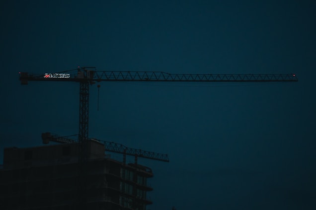 A sleek construction site at dusk featuring a black and gold crane against a city skyline.