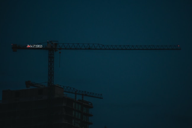 Team of engineers discussing plans in front of a large construction crane at dawn.