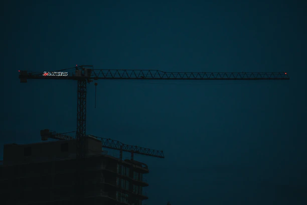 A rugged construction site at dusk with steel beams silhouetted against a darkening sky.
