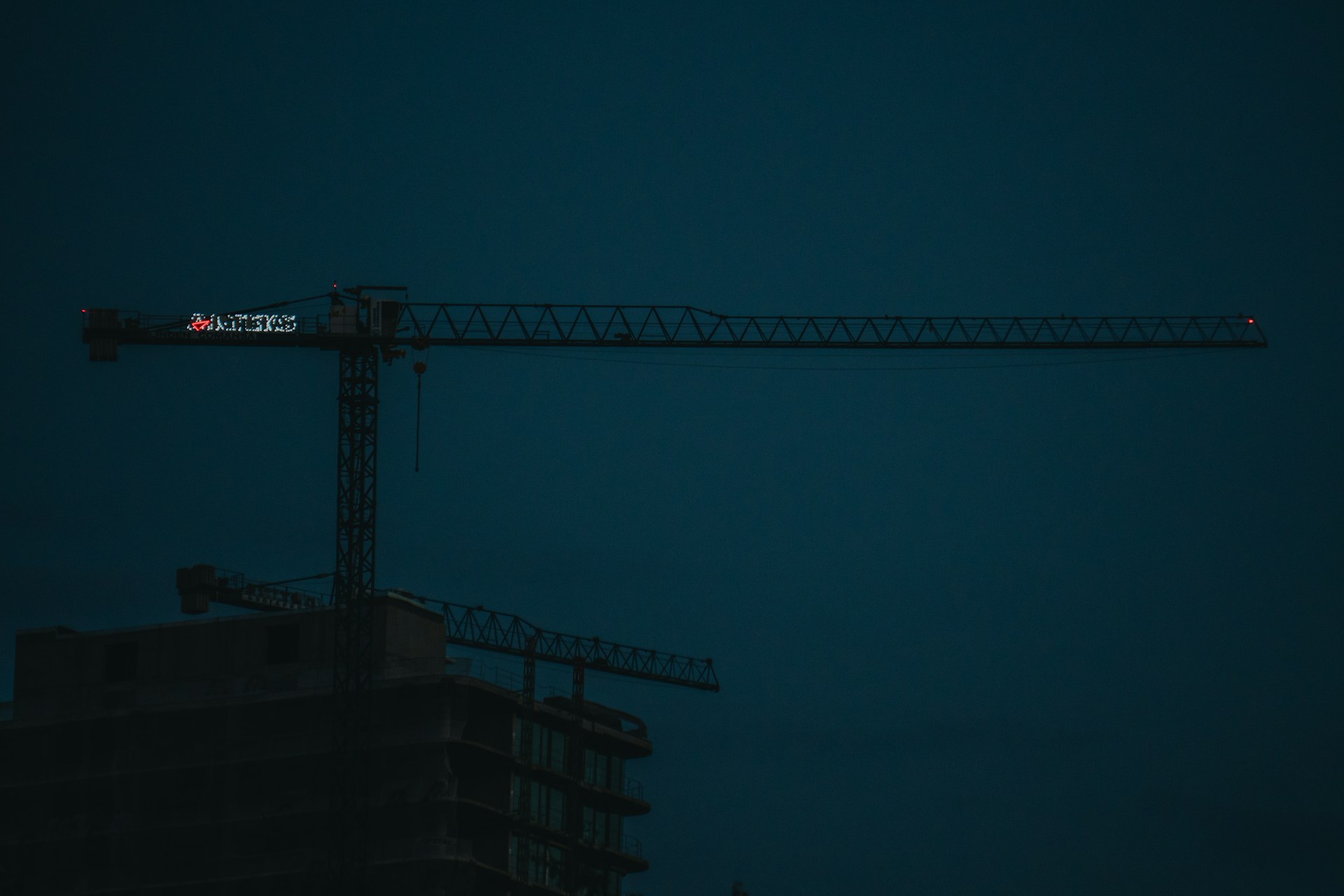 Cristian Anaya reviewing blueprints on a construction site at dusk, with dark tones and orange safety gear highlighting the scene.