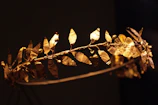 Craftsman’s hands delicately finishing a golden necklace inspired by laurel crowns.
