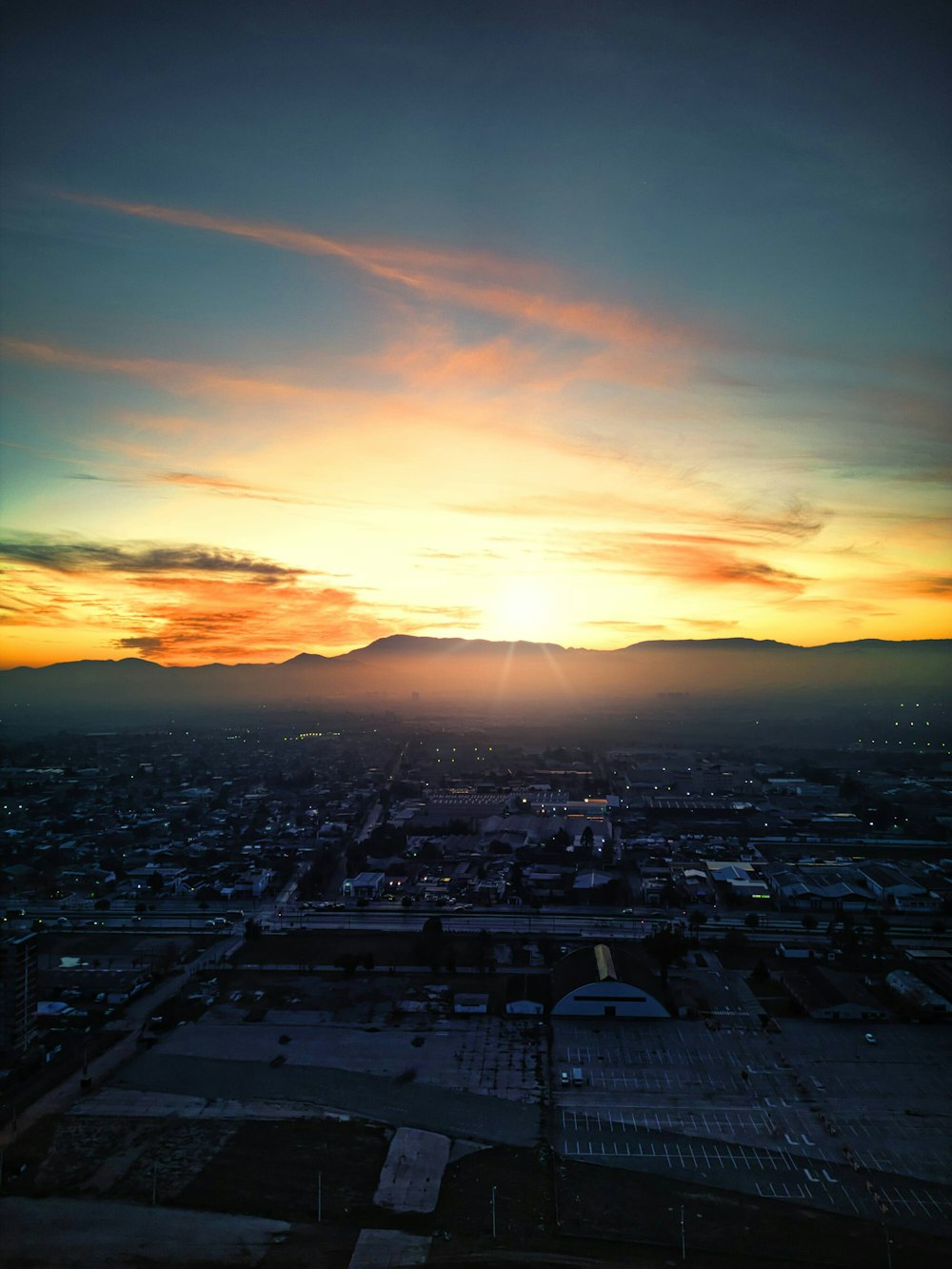 the sun is setting over a city with mountains in the background