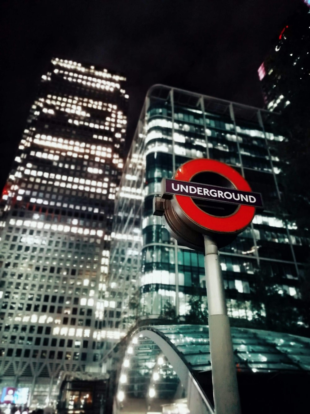 a red and black underground sign in front of a tall building