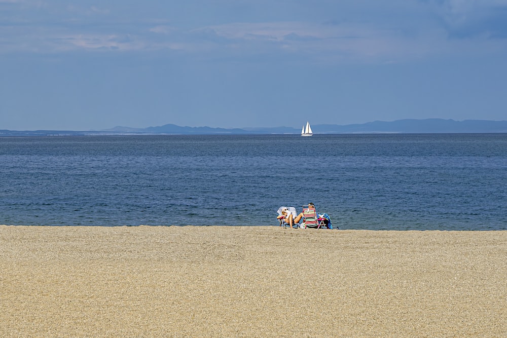 a couple of people sitting on top of a sandy beach