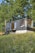 A cozy tiny house nestled in a lush green forest, showcasing its wooden exterior and large windows.