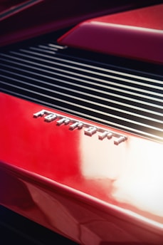 Close-up of a sleek red sports car grille gleaming under bright sunlight on a city street.