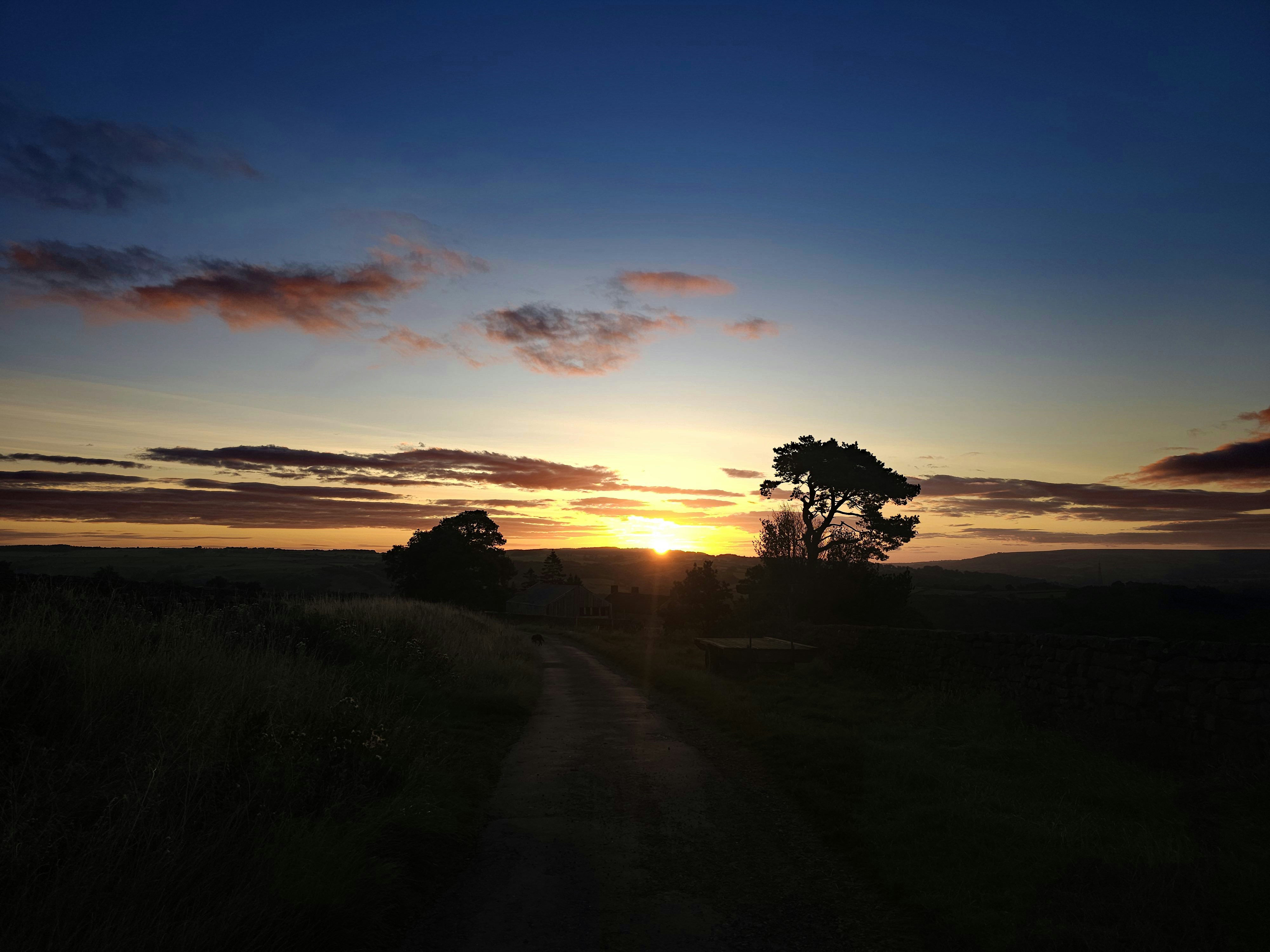 the sun is setting over a dirt road
