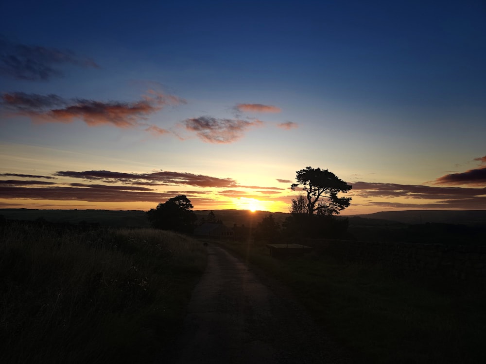 the sun is setting over a dirt road