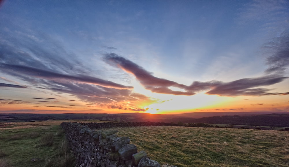 the sun is setting over a field with a stone wall