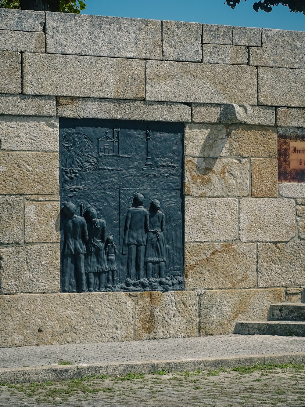 Una estatua de un grupo de personas de pie frente a un muro de piedra