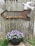 A close-up of a colorful garden sign hanging on a wooden fence with blooming flowers around.