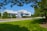 A modern college building is surrounded by lush greenery, including well-maintained lawns and trees. The structure features a sleek, white facade with large windows. Several cars are parked nearby, and a clear blue sky enhances the setting.