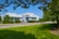 A modern college building is surrounded by lush greenery, including well-maintained lawns and trees. The structure features a sleek, white facade with large windows. Several cars are parked nearby, and a clear blue sky enhances the setting.