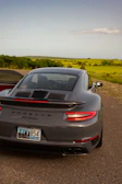 A Porsche 911 Turbo speeding along a coastal highway with a Cirrus SR22 soaring overhead.