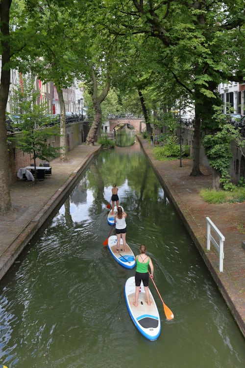 People stand-up paddleboarding (SUP) along a historic canal in Utrecht