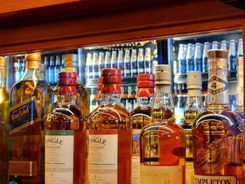Various whiskey bottles are displayed on a shelf in a liquor store, showcasing different brands and labels. The bottles are arranged in a row, with visible labels such as Dingle, Blue Label, and Templeton. The background features more bottles, reflecting a well-stocked display of alcoholic beverages.