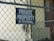 A chain-link fence is prominently featured with a sign that reads 'PRIVATE PROPERTY NO TRESPASSING' attached to it. Behind the fence, there is a building with beige siding and a small railing visible.
