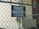 A chain-link fence is prominently featured with a sign that reads 'PRIVATE PROPERTY NO TRESPASSING' attached to it. Behind the fence, there is a building with beige siding and a small railing visible.