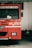 A red fire truck is parked indoors. The vehicle has various labels, including 'FIRE' and a license plate marked 'KA-01 G-8091'. Around the truck, other objects such as helmets and another vehicle can be seen.