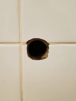 Close-up of a technician carefully repairing a small hole in a bathroom tile with specialized tools.