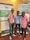 Three individuals are standing in front of two vertical banners related to Makerere University. They are smiling and appear to be at an event or conference. The individuals are wearing casual clothes and have name tags around their necks.