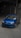 A blue Volkswagen car is parked in a dimly lit garage with a sloped concrete floor. The car is a sporty hatchback model with sleek design features, including a sunroof and alloy wheels.
