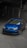 A blue Volkswagen car is parked in a dimly lit garage with a sloped concrete floor. The car is a sporty hatchback model with sleek design features, including a sunroof and alloy wheels.