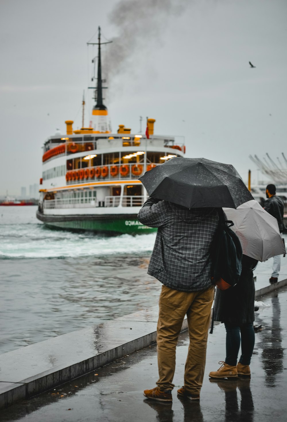 Un couple de personnes avec des parapluies regardant un bateau