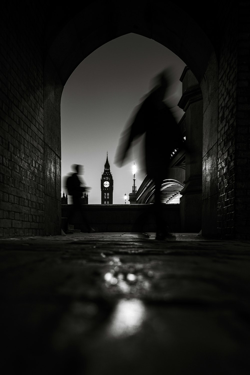 a black and white photo of a person walking under a bridge