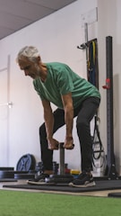 An elderly man doing a gentle strength exercise with light weights at home.