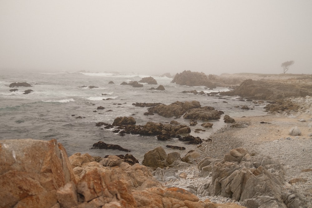a foggy day at the beach with rocks and water