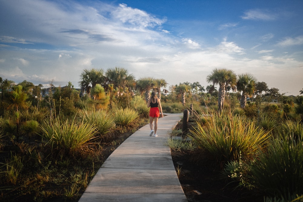 a woman walking down a path through a lush green field