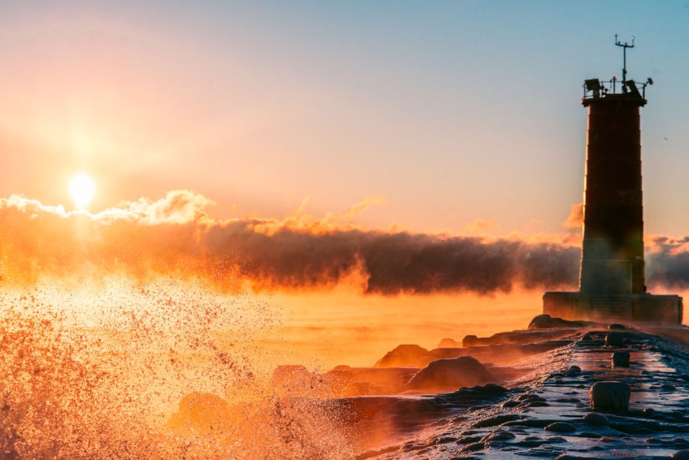 the sun is setting behind a lighthouse on the water