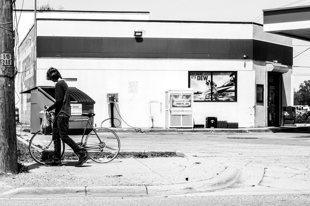 um homem andando de bicicleta por uma rua ao lado de um posto de gasolina