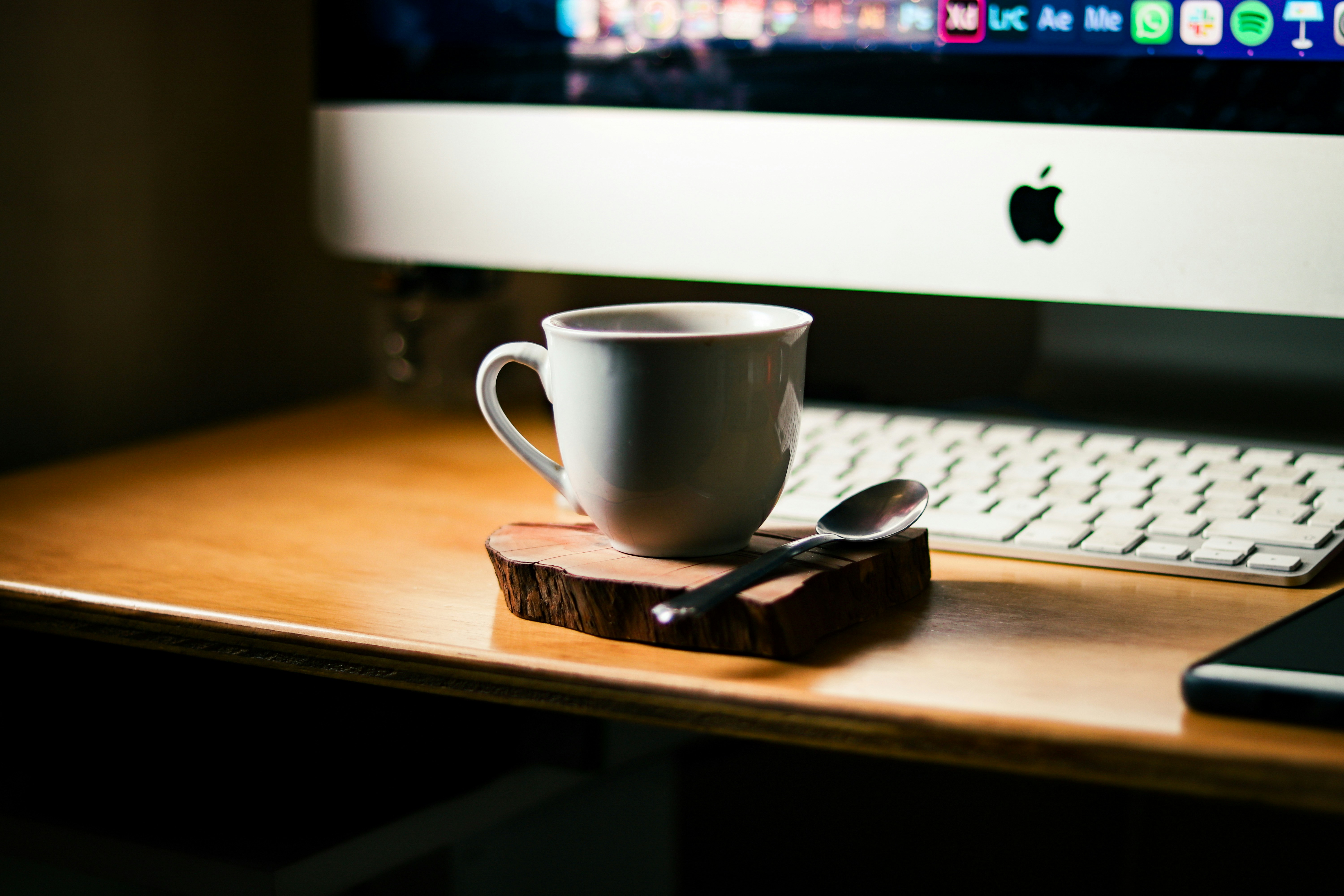 a cup of coffee on a wooden coaster next to a computer