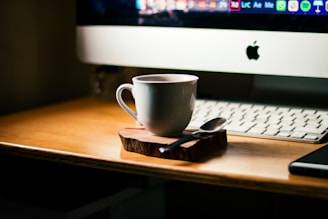 a cup of coffee on a wooden coaster next to a computer
