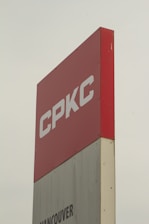 A tall sign with the letters 'CPKC' in bold white font on a red background. Below it, there is a partial view of a grey section with the text 'Vancouver'. The sign has a clean, modern appearance and stands against a cloudy sky.