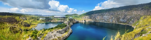 A panoramic view of a sunlit quarry with layers of green stone and smooth river rocks.